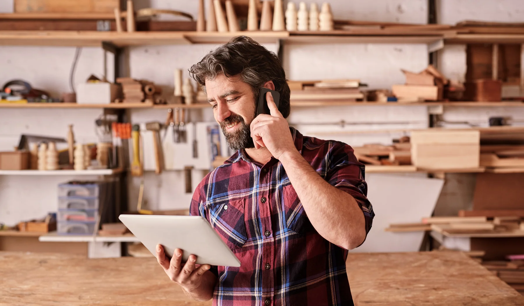 Craftsperson using a phone and tablet in a woodworking shop.